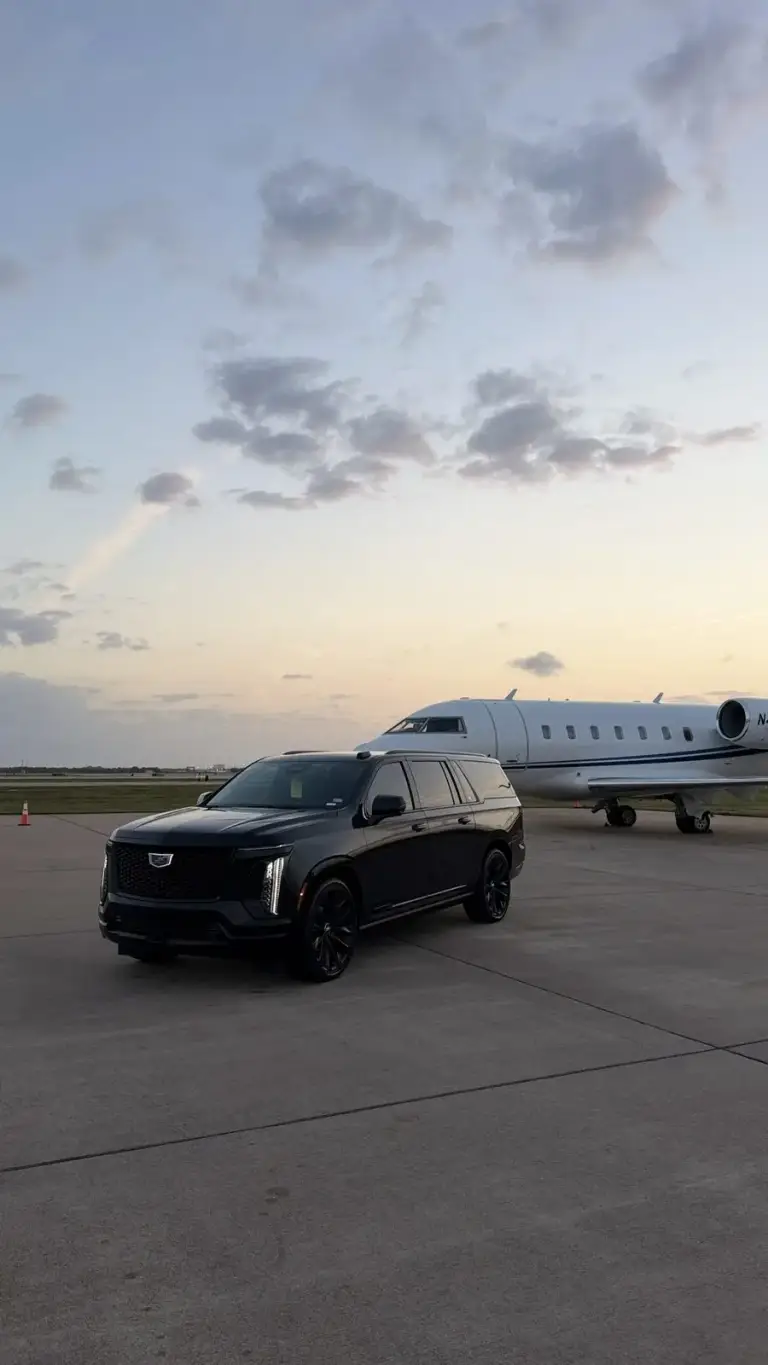 Black Cadillac Escalade-V on an airport ramp beside a private jet at sunset